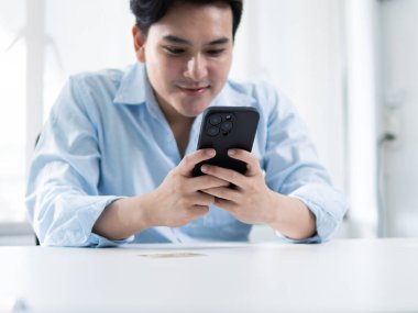 Mobil teknolojiyle ilgilenen genç adam akıllı telefon, modern ofis, dijital iletişim, parlak çevre, yakın çekim, bağlantı kavramı kullanıyor.