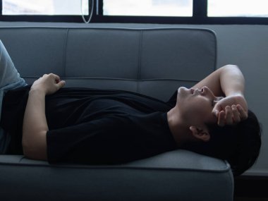 Modern bir oturma odasındaki kanepede dinlenen genç bir adamın düşünceli anı zihinsel sağlık farkındalığı için düşünceli bir bakış açısı.