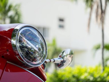 Kırmızı bir scooter 'ın farının büyüleyici bir yakın çekimi. Şatafatlı bir şehir ortamında tasarımını sergiliyor..