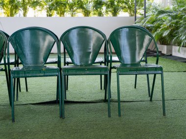 Bereketli yeşilliklerle çevrili yeşil sandalyeler içeren sakin bir açık hava ortamı..