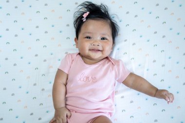 Neşeli bir Asyalı yeni doğmuş bebek, parlak bir şekilde gülümsüyor. Masumiyet ve sıcaklığı, kapalı bir ortamda yayıyor..