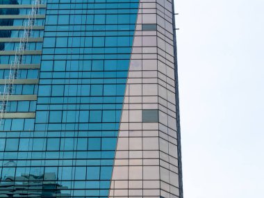 Çarpıcı bir modern gökdelen, kentsel bir manzaranın ortasında cam cephesinde yansımalarını sergiliyor.