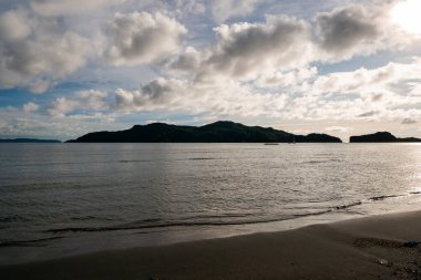 Sakin okyanus dalgalarının sakin güzelliğini keşfedin bulutlu bir gökyüzünün altındaki tropik bir adaya çarpan.