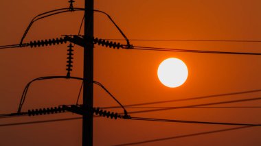 Büyüleyici bir günbatımı enerji altyapısını vurgulayan elektrik hatlarının üzerine sıcak bir ışık saçar..