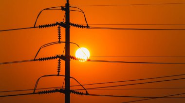 Çarpıcı bir günbatımı, şehir manzarası boyunca uzanan elektrik hatlarıyla gökyüzünü boyuyor..