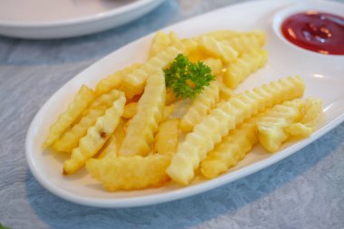 Altın kıvrımlı patates kızartması ketçapla servis edilir. Lezzetli bir atıştırmalık deneyimi sunar..