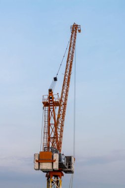 Yüksek bir inşaat vinci, gökyüzüne karşı modern endüstriyel operasyonlar sergiliyor.