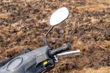 Kırsal bir alanın arka planına karşı motosiklet gidonunun yakın plan görüntüsü karmaşık ayrıntıları vurguluyor.