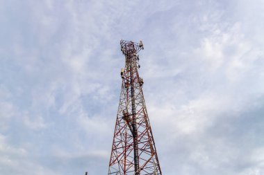 Bir telekomünikasyon kulesi bulutlu bir gökyüzüne karşı ayakta duruyor. Şehir altyapısını ve teknolojik gelişmeleri gösteriyor..