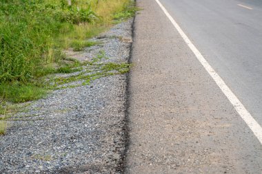 Sakin bir yol kenarı manzarası kırsal alanda yemyeşil çimlerin yanında çakıllar sergiliyor..