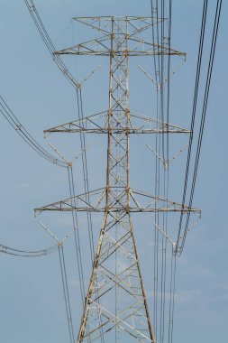 Yüksek bir elektrik iletim hattı, kentsel alanlardaki enerji dağılımını sembolize eden açık mavi gökyüzüne karşı duruyor..