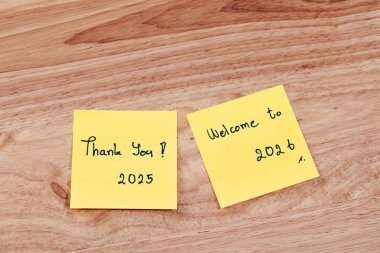 Yapışkan notlar teşekkürlerini sunuyor. 2025 ve 2026 'ya hoş geldiniz. Sıcak çalışma alanındaki umut ve taze başlangıçları simgeleyen yapışkan notlar..