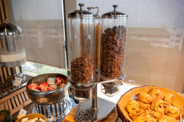 Canlı bir kahvaltı büfesi. Çeşitli lezzetli yemek seçenekleri var. Misafirleri memnun etmeye davet ediyorlar..