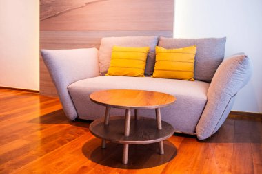 Sarı yastıklı şık gri bir kanepe ve sıcak bir dairede yuvarlak bir sehpa..