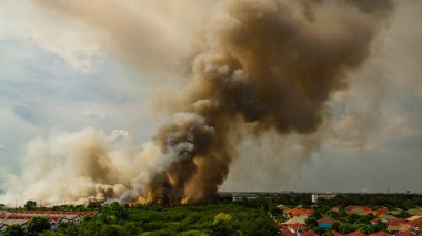 Çarpıcı bir alev, çevresel zorlukları vurgulayan şehir manzarası üzerinde yükselen bir duman bulutu oluşturur..