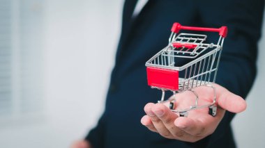 Bir işadamı, e-ticareti ve perakende yeniliği sembolize eden modern ofis ortamını simgeleyen küçük bir alışveriş arabasını sergiliyor..