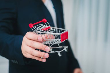 Bir işadamı, perakende stratejisini sembolize eden bir alışveriş arabası sunar. Modern bir bağlam..