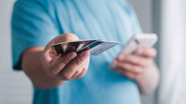 Bir kişi dijital ödeme işlemini tamamlamak için akıllı telefon kullanırken kartları teslim eder.