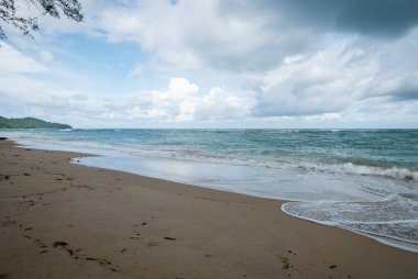 Hafif dalgaların bulutlu bir gökyüzünün altında güzel bir tropikal plaja vurduğu huzuru hissedin..