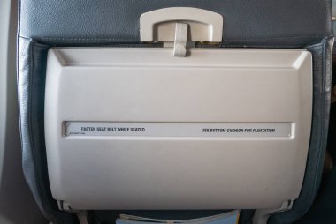 Uçak tepsisi sehpasında uçuş sırasında yolcu yönlendirmesi için güvenlik talimatları yer alıyor.