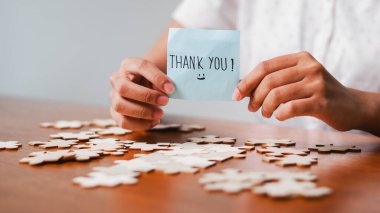 Dağınık yapboz parçalarının arasında bir teşekkür notu tutan yakın çekim..