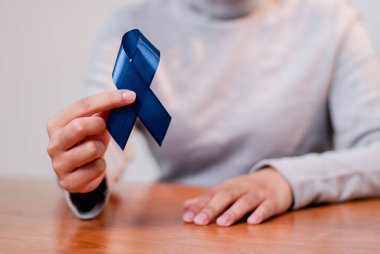 Sağlık farkındalığını sembolize eden mavi kurdeleli bir kişinin yakın plan fotoğrafı..