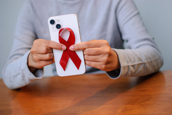 A person holds a smartphone adorned with a red ribbon symbolizing support for HIV/AIDS awareness.
