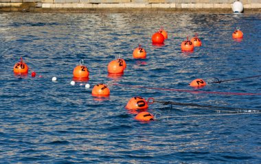 Bir rıhtımın yanındaki deniz suyunda turuncu renkli şamandıra sürüsü.