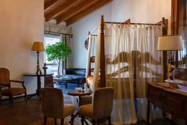 Açık alan iç dekorasyonu klasik tarzda mobilyalar, bir masa ve ön planda dört posterli yatak ve arka planda pencerenin yanında bir kanepe ile dekore edilmiş. 