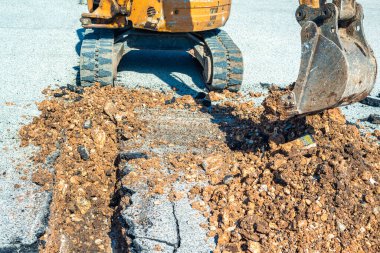 Small excavator with narrow bucket in action for the construction of a channel on a building site