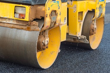 Yeni asfaltı düzleştiren bir paten sıkıştırıcısı olan yol inşaatı. Makineye yakın çekim, kaldırım sürecini vurguluyor.
