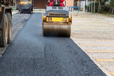 Yeni asfaltı düzleştiren bir paten sıkıştırıcısı olan yol inşaatı. Makineye yakın çekim, kaldırım sürecini vurguluyor.