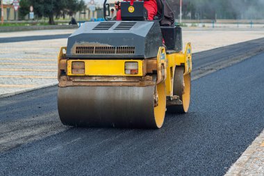 Yeni asfaltı düzleştiren bir paten sıkıştırıcısı olan yol inşaatı. Makineye yakın çekim, kaldırım sürecini vurguluyor.