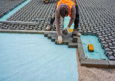İnşaat alanına birbirine kenetlenmiş beton kaldırımlar yerleştiriliyor. Döşeme işlemine yakın plan, desen ve dokuyu vurguluyor.