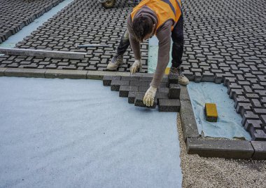İnşaat alanına birbirine kenetlenmiş beton kaldırımlar yerleştiriliyor. Döşeme işlemine yakın plan, desen ve dokuyu vurguluyor.