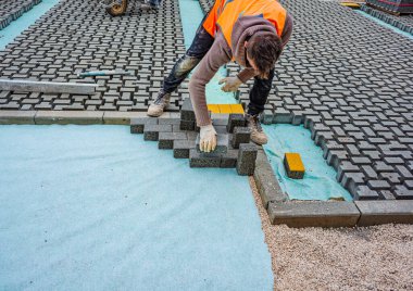 İnşaat alanına birbirine kenetlenmiş beton kaldırımlar yerleştiriliyor. Döşeme işlemine yakın plan, desen ve dokuyu vurguluyor.