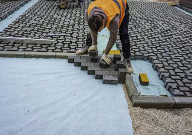 İnşaat alanına birbirine kenetlenmiş beton kaldırımlar yerleştiriliyor. Döşeme işlemine yakın plan, desen ve dokuyu vurguluyor.