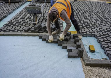 İnşaat alanına birbirine kenetlenmiş beton kaldırımlar yerleştiriliyor. Döşeme işlemine yakın plan, desen ve dokuyu vurguluyor.