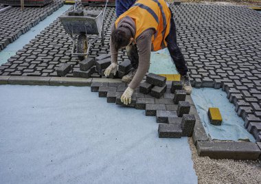 İnşaat alanına birbirine kenetlenmiş beton kaldırımlar yerleştiriliyor. Döşeme işlemine yakın plan, desen ve dokuyu vurguluyor.