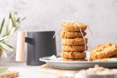 Stack of homemade oatmeal cookies, healthy breakfast cereal oat crackers and mug of milk with coffee on white kitchen countertop