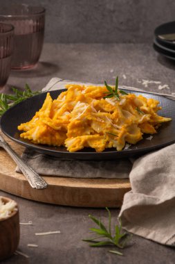 Balkabağı soslu Farfalle makarna ve siyah seramik tabakta biberiyeyle süslenmiş parmesan peyniri. Kremalı vejetaryen vejetaryen kabaklı makarna. Mutfak tezgahı..