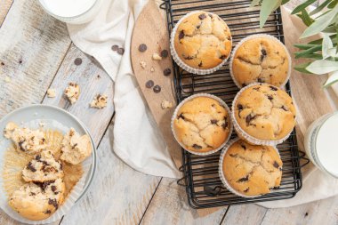 Chocolate chip muffins on a baking rack and glasses of milk on a white kitchen countertop.  Morning breakfast table. Top view, flat lay