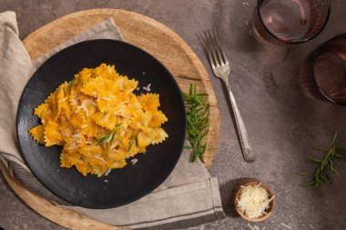 Balkabağı soslu Farfalle makarna ve siyah seramik tabakta biberiyeyle süslenmiş parmesan peyniri. Kremalı vejetaryen vejetaryen kabaklı makarna. Mutfak tezgahının üstü. Üst Manzara. Düz yatıyordu