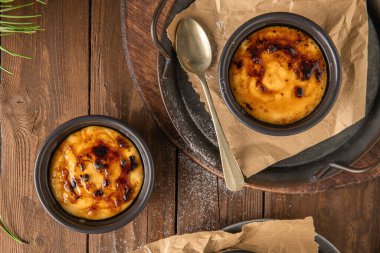 Creme brulee. Üzerinde karamelize şeker olan vanilyalı Fransız tatlısı, kaşıklar, koyu kırsal masa. Leit kreması, Portekiz çölü creme brulee, creme brulee ve creme brulee 'ye benzer..