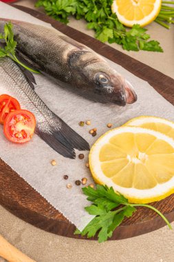 Taze çiğ deniz levreği, limon dilimleri, maydanoz, ahşap masada kırmızı biber ve tuz, yakın plan.