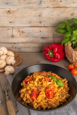 Fusilli pasta with tuna in tomato sauce in a skillet on a dark grey slate, stone or concrete background. Top view with copy space.