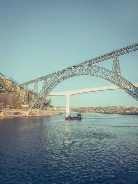 Douro river with traditional sailing wine boat cruise, view of Maria Pia and Sao Joao bridges, typical architecture of cascade housing in sunhine. Rabelo boat in douro river, Porto, Portugal