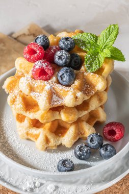 Geleneksel Belçika waffleları, mutfak tezgahına taze ahududu ve yabanmersini serpiştirilmiş pudra şekeri serpiştirilmiş..