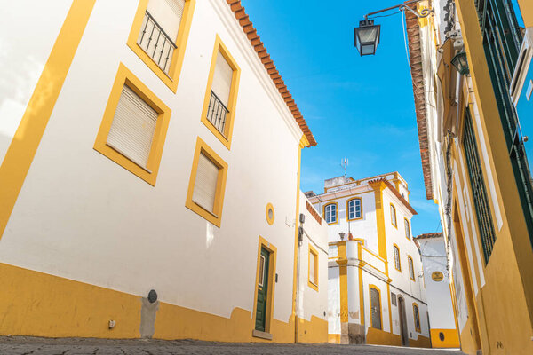 The view of narrow paved street of Evora with the cozy white and yellow houses. Evora. Alentejo. Portugal