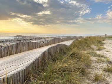 Günbatımında parlayan Furadouro sahiline kumsal erişimi sağlayan bir kum tepeciği üzerine inşa edilmiş bir orman yaya geçidi. Ovar, Aveiro, Portekiz, Avrupa